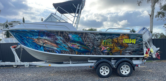 Boat with colorful boat wrap graphics on a trailer, parked on grass with a cloudy sky.